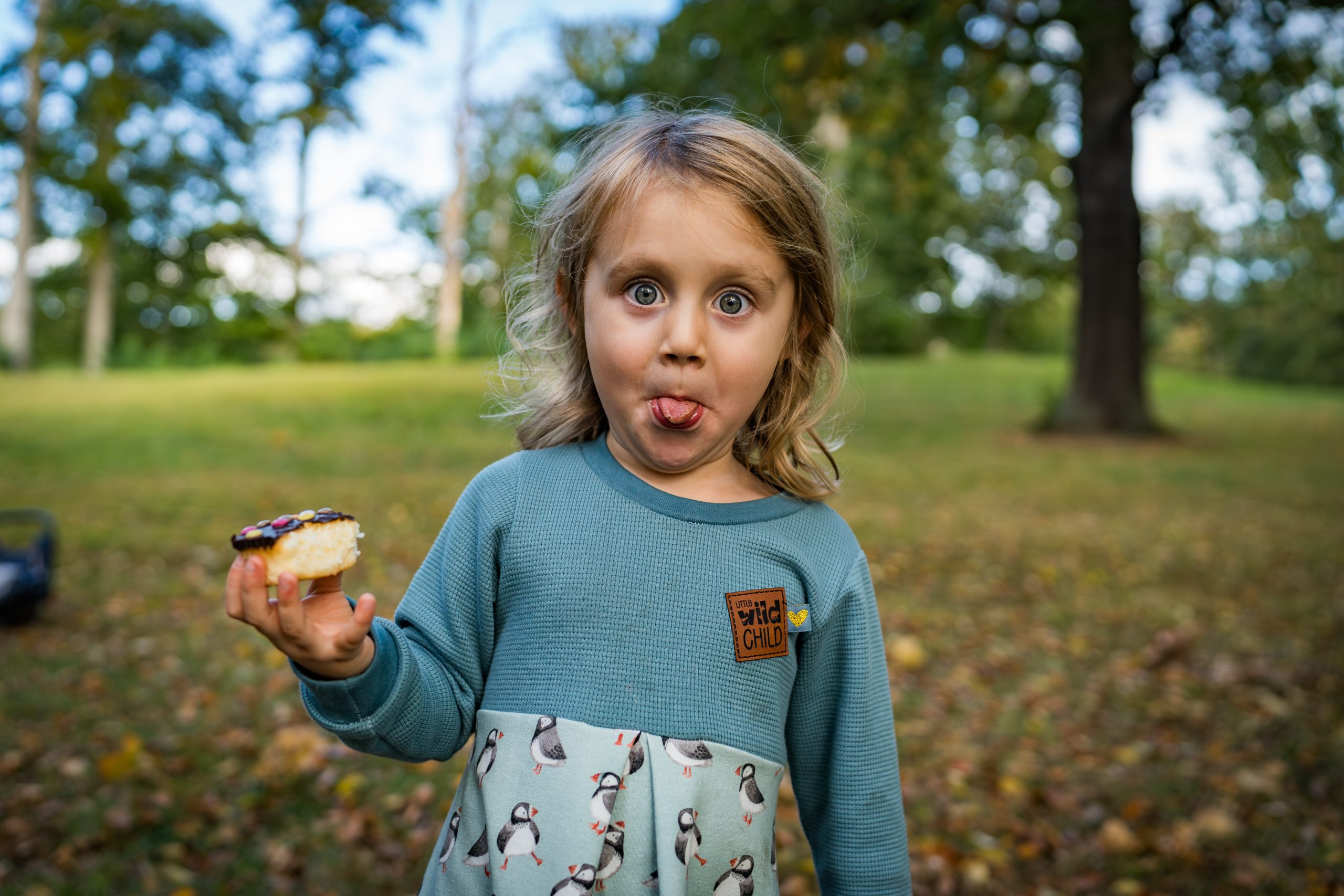 Portrait eines Kindes, das einen Muffin in der Hand hält, große Augen macht und der Kamera die Zunge herausstreckt